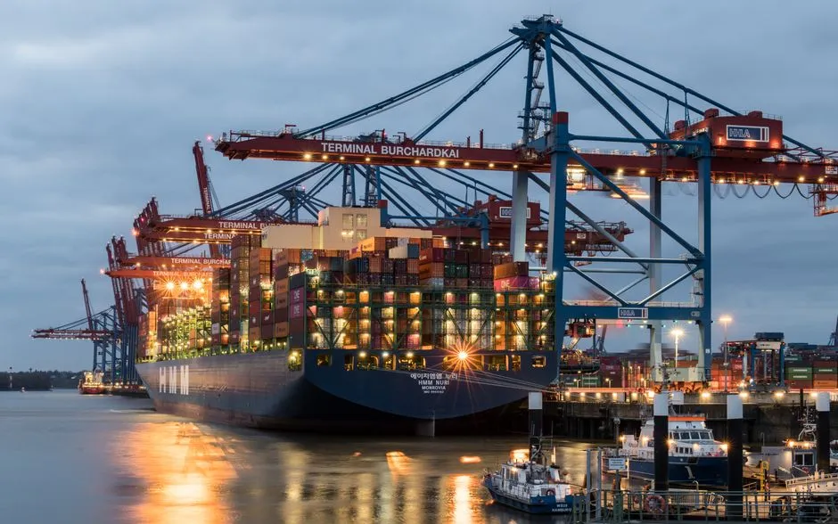 Porte-conteneurs à quai sous les grues d'un terminal portuaire au crépuscule, illustrant les importations soumises à l'octroi de mer et la vie chère en Martinique