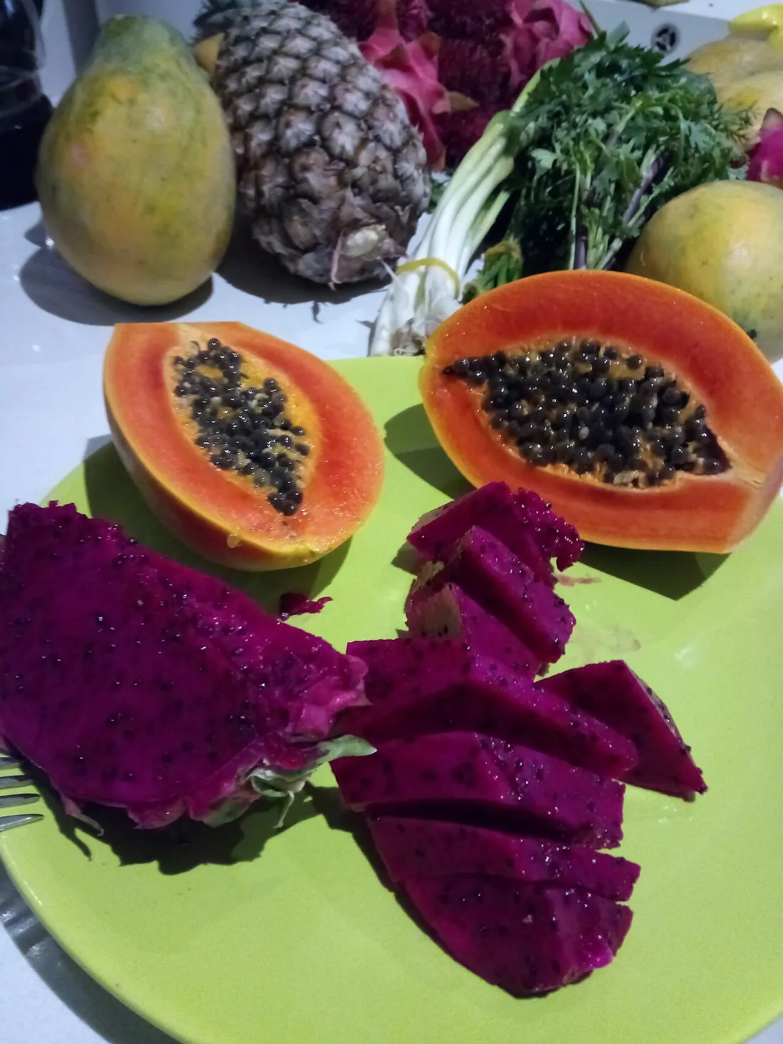 Etal de fruits tropicaux au marche de Cayenne : papaye coupee, ananas et pitaya rouge sur une assiette verte