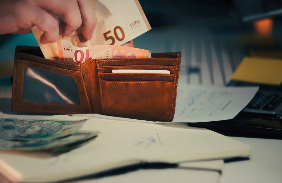 Portefeuille avec billets en euros posé sur un bureau avec documents et calculatrice, évoquant un paiement par virement en euros