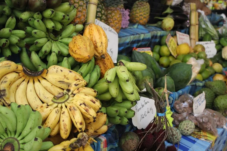 Etal de marche antillais avec bananes, plantains, cabosses de cacao, citrons verts et fruits-pays accompagnes d'etiquettes de prix au kilo en euros