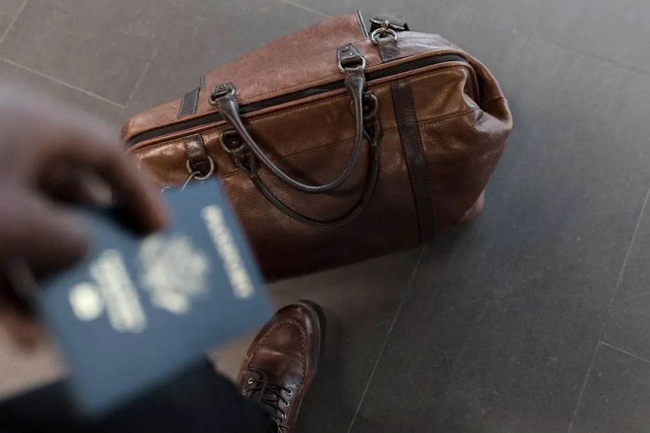Voyageur tenant son passeport à côté d'un sac de voyage en cuir, prêt au départ à l'aéroport