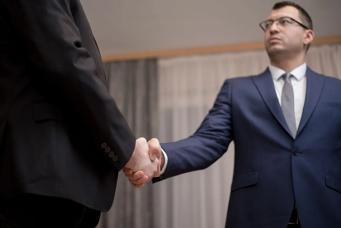 Deux professionnels en costume se serrant la main lors d'un rendez-vous d'affaires, illustrant une relation entre prestataire et entreprise cliente