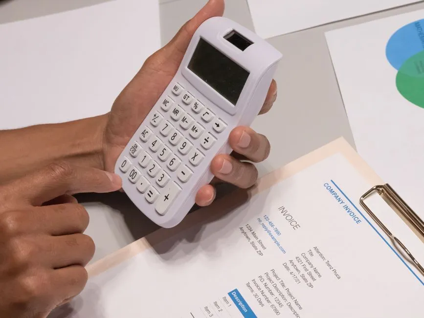 Mains tenant une calculatrice au-dessus d'une facture d'entreprise détaillée posée sur un bureau