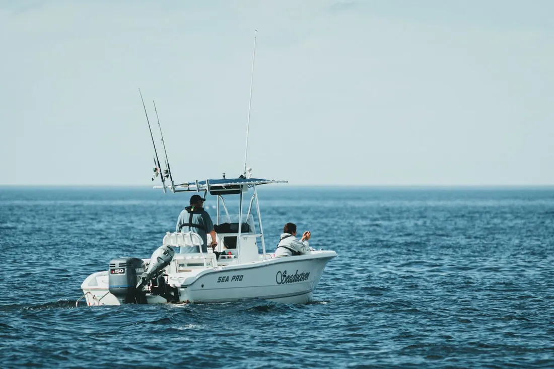 Bateau de pêche sportive avec cannes sur portiques et deux pêcheurs au large, sur la mer ouverte