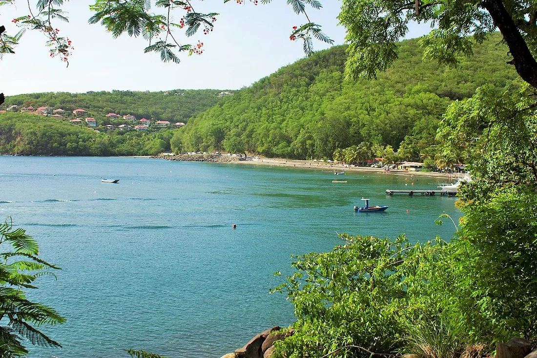 Baie de la plage de Malendure à Bouillante, avec bateaux amarrés et ponton devant la côte sous-le-vent boisée de Guadeloupe