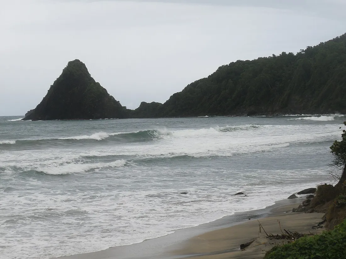Anse Charpentier sur la côte Nord Atlantique sauvage de la Martinique à Sainte-Marie, avec son rocher emblématique au large et les vagues de l'Atlantique sur le sable sombre