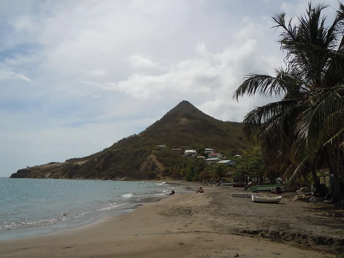 Plage de sable de Petite Anse aux Anses-d'Arlet, sur la côte Caraïbe de la Martinique, avec cocotiers, barques de pêcheurs et morne en arrière-plan