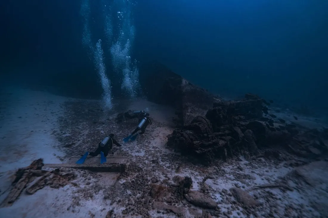 Deux plongeurs en bouteille explorant une épave reposant sur un fond sableux en eau profonde
