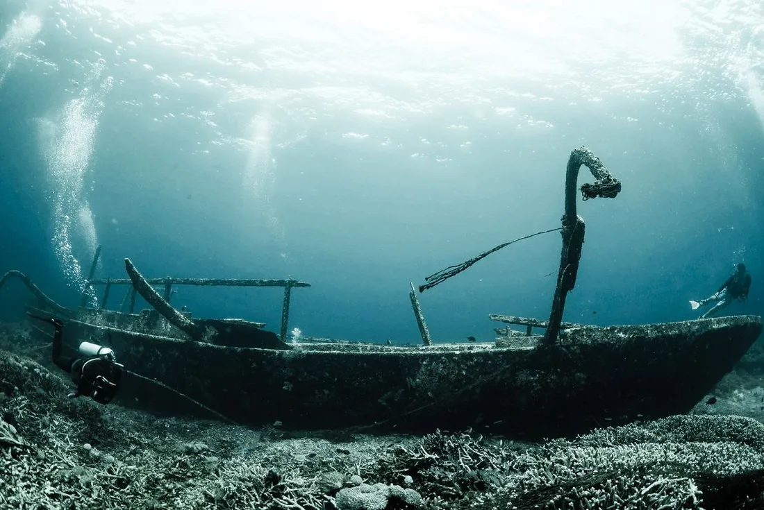 Plongeur longeant la coque d'un bateau coulé sous une eau claire baignée de lumière