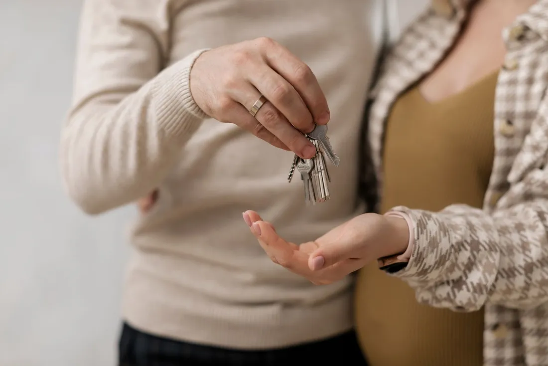 Gros plan sur une remise de clés : une main tend un trousseau de clés de logement au-dessus de la paume ouverte d'une autre personne
