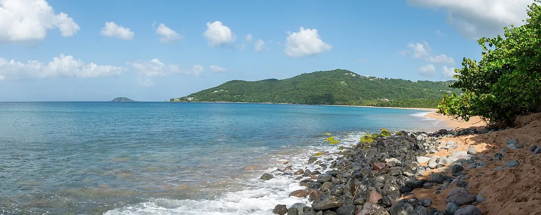 Baie de Grande Anse a Deshaies en Guadeloupe, collines verdoyantes et mer des Caraibes sous un ciel partiellement nuageux