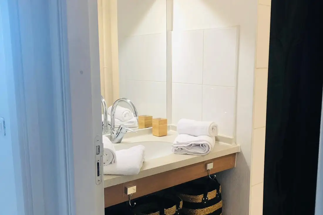 Salle d’eau du Diamant Cayennais : serviettes blanches roulées sur la vasque, boîte en bambou et paniers de rangement