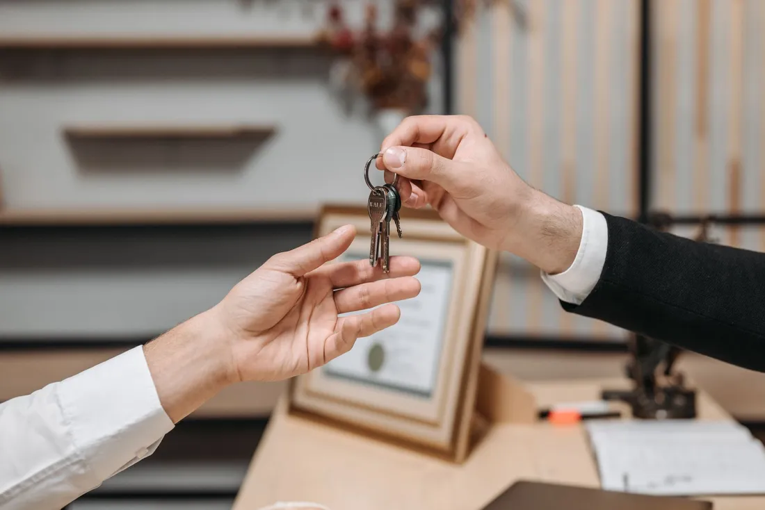 Remise d'un trousseau de clés d'une main à une autre au-dessus d'un bureau, symbolisant la restitution du logement à la fin du bail