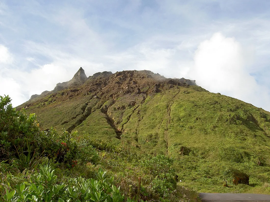 Le dôme sommital de la Soufrière (1467 m) en Guadeloupe, coiffé de nuages et de brume, dominant les pentes vertes au-dessus du sentier