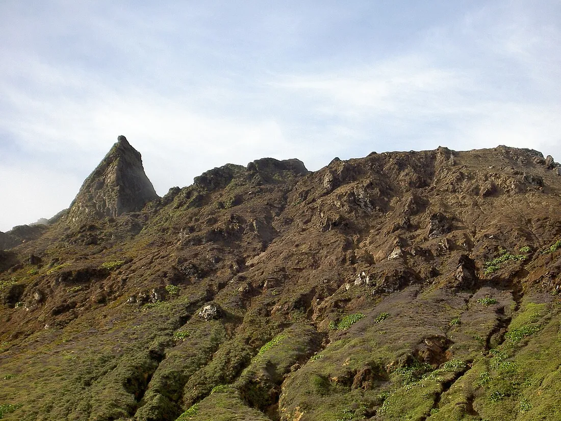 Sommet rocheux de La Soufrière (1467 m) en Guadeloupe, avec un piton de roche volcanique dressé au-dessus des pentes couvertes de végétation rase