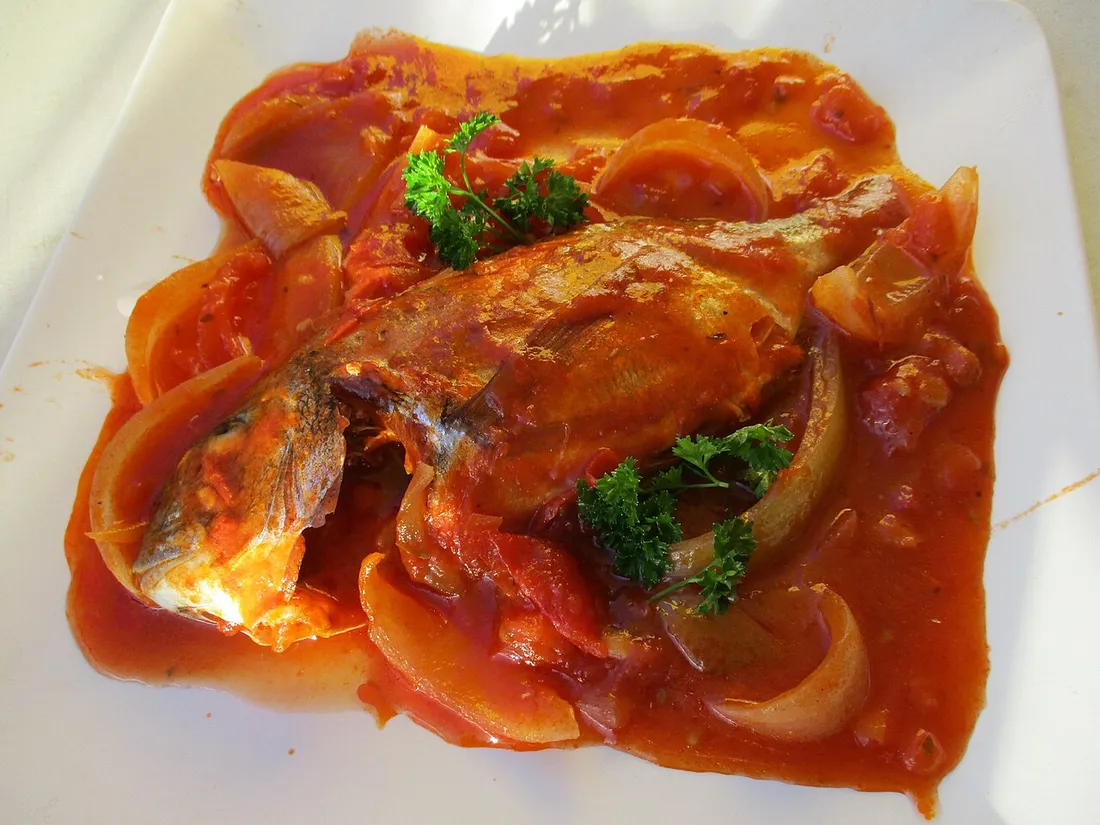 Court-bouillon de poisson antillais : poisson entier nappé de sauce tomate créole avec oignons et persil, dressé dans une assiette