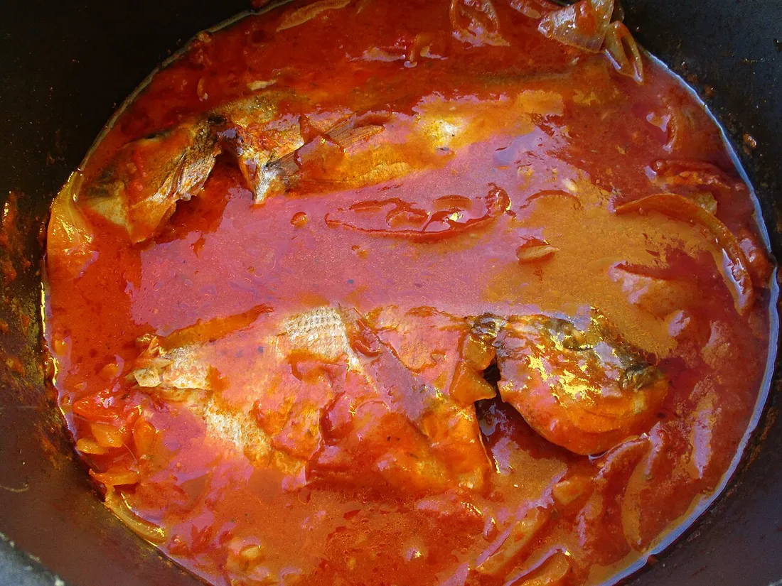 Morceaux de poisson mijotant dans une sauce tomate épicée au fond d'une marmite, façon court-bouillon créole