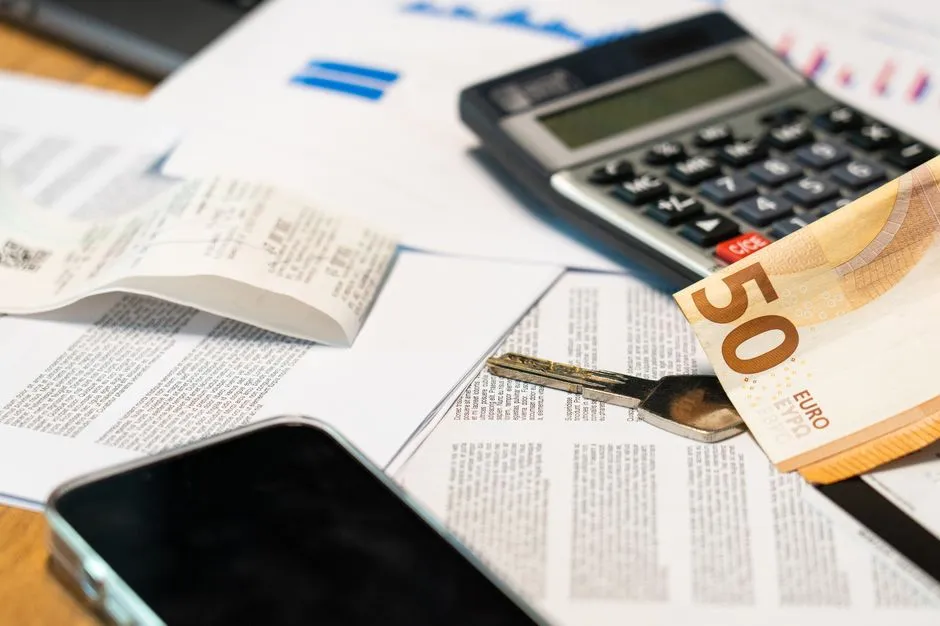Calculatrice, billet de 50 euros et clé posés sur des documents et graphiques financiers pour calculer un rendement locatif