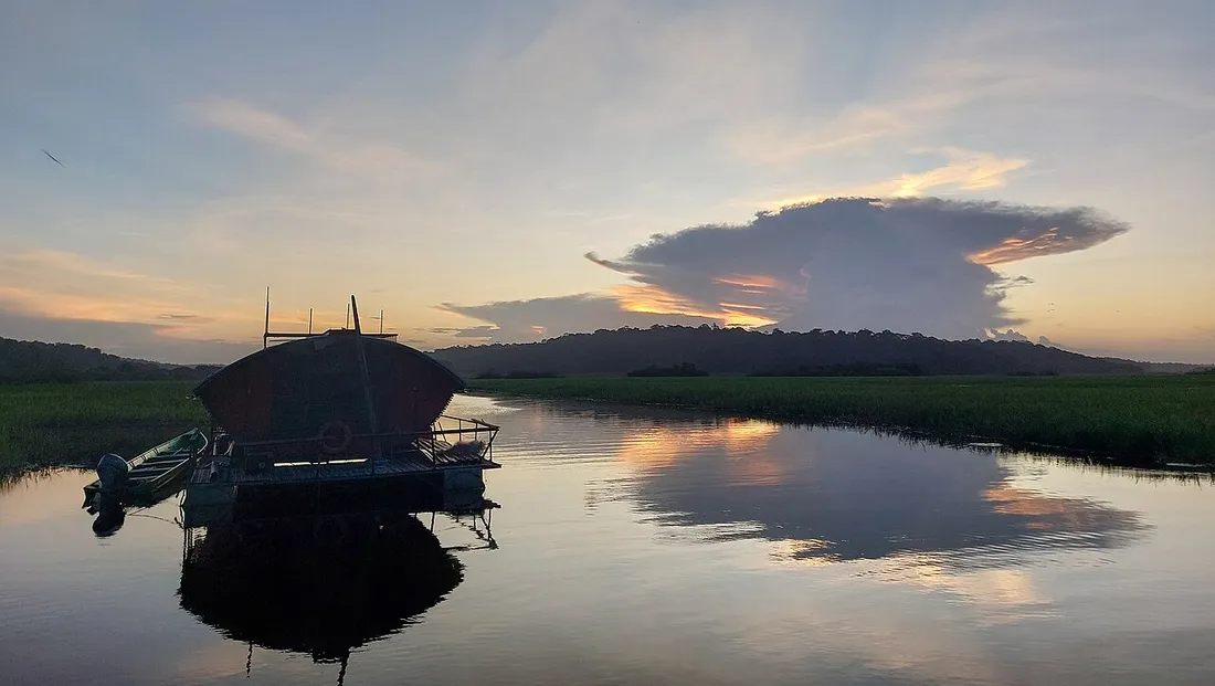 Carbet flottant amarré sur l'eau au coucher du soleil dans les marais de Kaw, en Guyane, avec reflets et ciel orangé