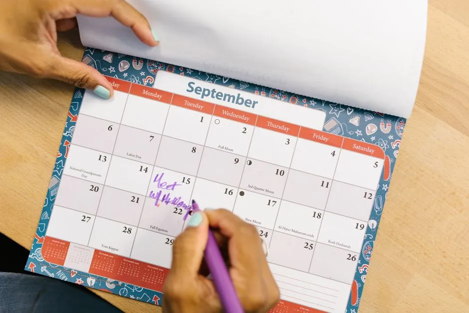 Main annotant au feutre violet une date sur la page de septembre d'un calendrier posé sur une table