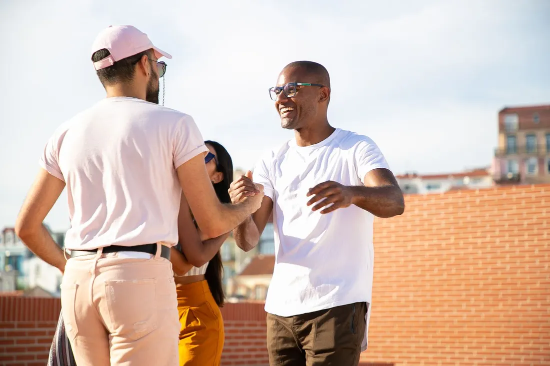 Groupe d'amis souriants d'origines diverses qui se saluent et se serrent la main en exterieur dans un cadre urbain ensoleille