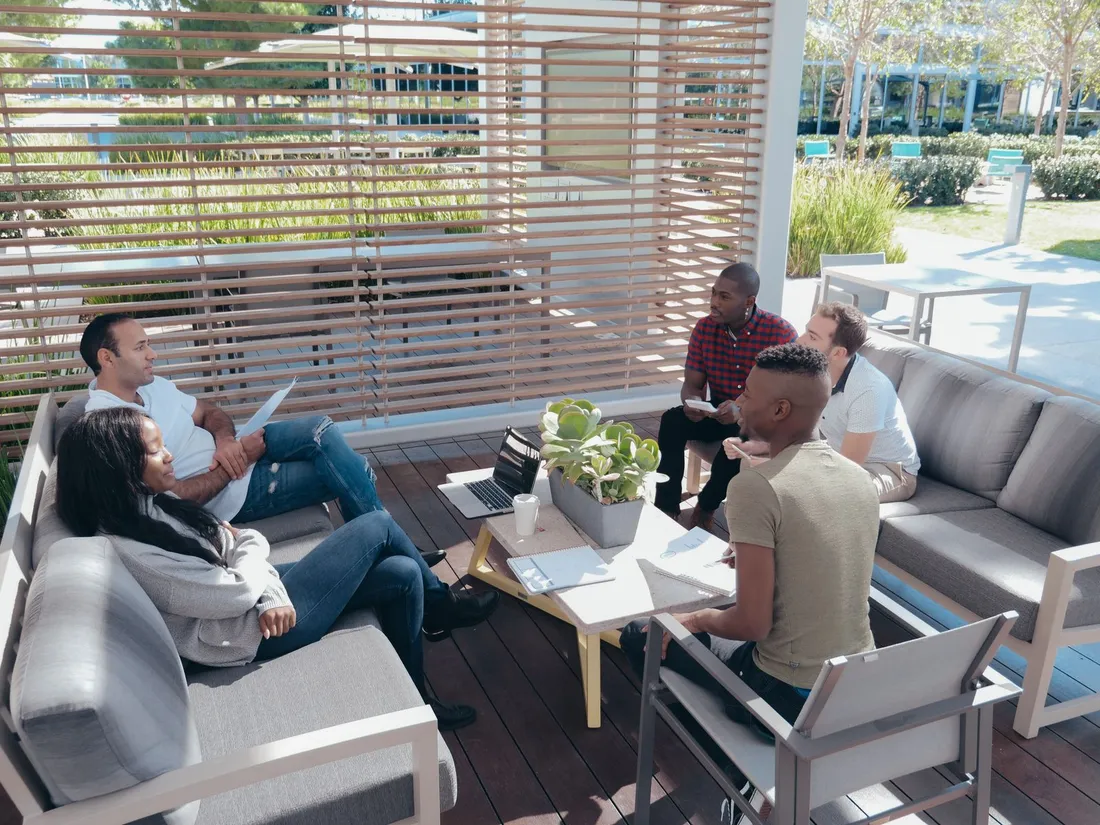 Groupe de collaborateurs d'une même entreprise réunis autour d'un ordinateur portable sur une terrasse ombragée en extérieur