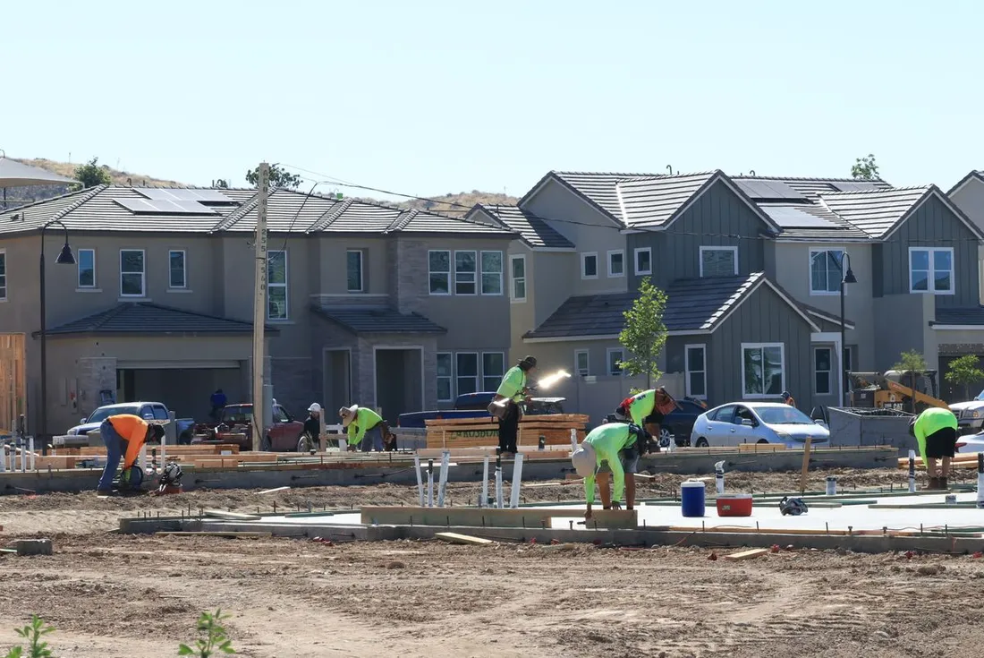 Ouvriers en gilets fluorescents travaillant sur les fondations d'un lotissement, devant une rangée de maisons neuves déjà achevées