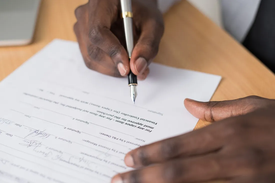 Gros plan sur les mains d'une personne signant un document imprimé posé sur une table en bois, stylo plume à la main