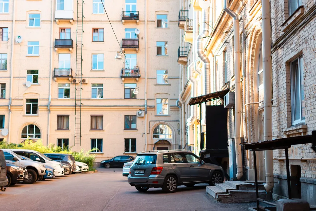 Cour de stationnement d'un ensemble de logements collectifs, voitures rangées le long de la façade et voie d'accès en impasse