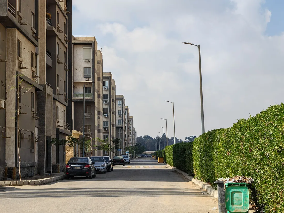 Rue bordée d'immeubles de logements de plusieurs étages aux façades vieillies, voitures stationnées le long du trottoir