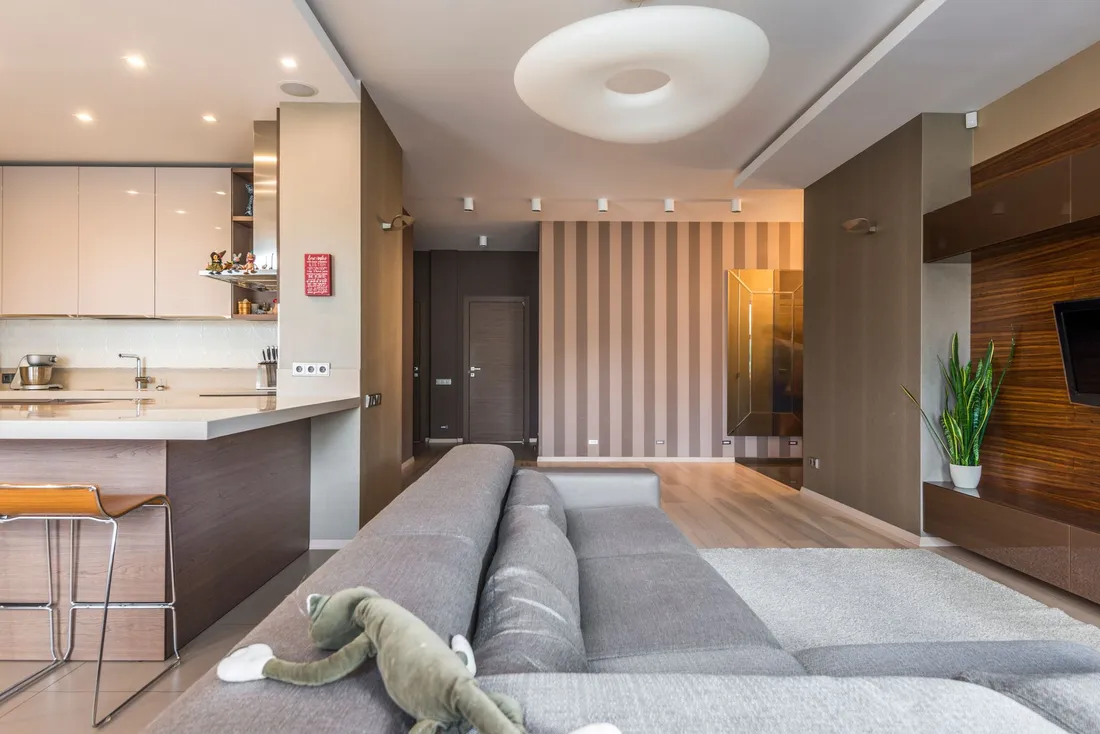 Séjour meublé d'un appartement avec canapé d'angle, cuisine ouverte et coin repas
