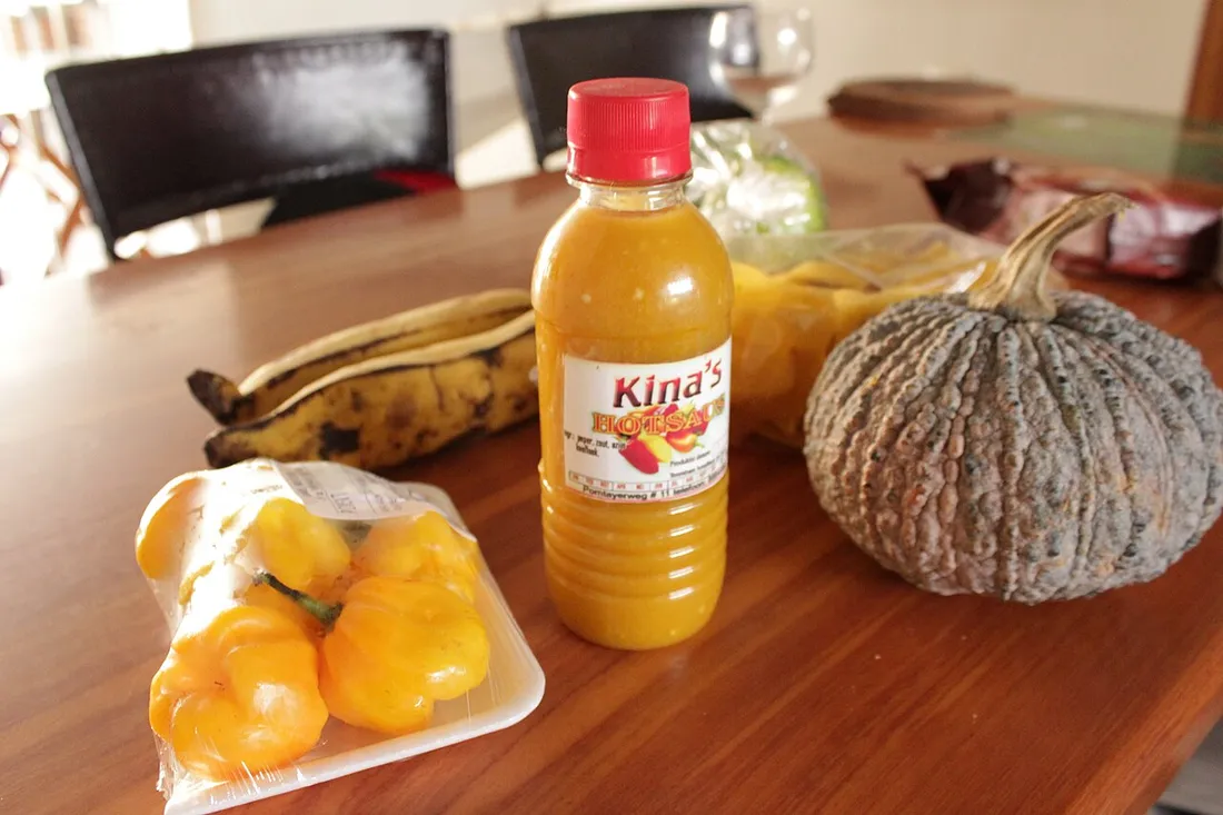 Produits locaux du marché de Cayenne en Guyane : bananes plantains, piments antillais, sauce piquante et giraumon posés sur une table