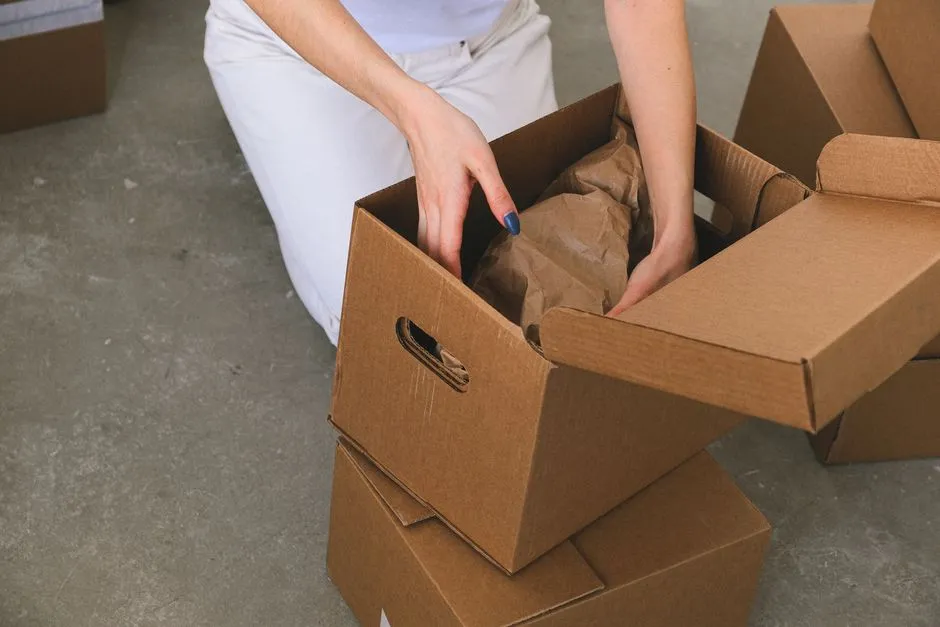 Personne agenouillée emballant des affaires dans un carton de déménagement, entourée d'autres cartons prêts à être fermés