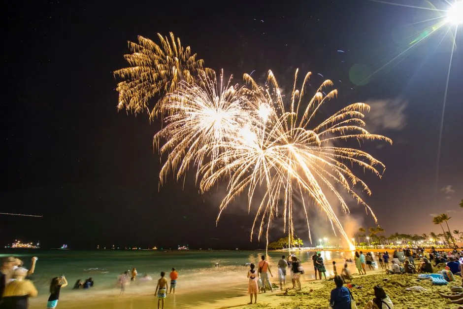 Feu d'artifice illuminant le ciel au-dessus d'une plage tropicale la nuit, devant une foule rassemblée sur le sable pour célébrer le réveillon