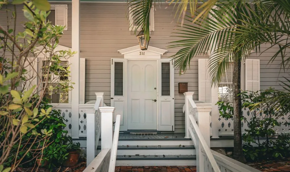 Façade et entrée d'une maison de style créole antillais avec terrasse en bois blanc, évoquant un bien immobilier mis en vente