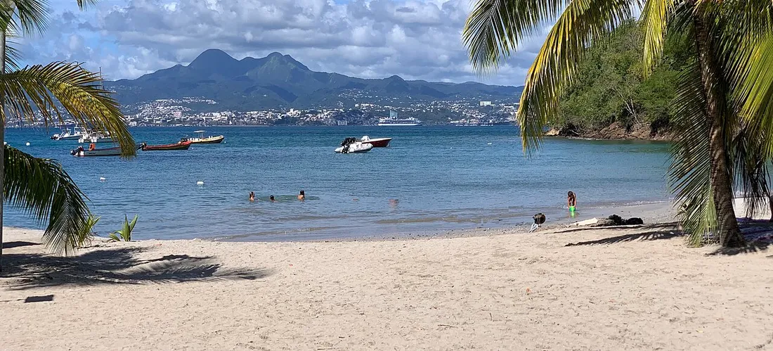 Baie de Fort-de-France en Martinique par temps ensoleillé, plage de sable, bateaux et pitons du Carbet en arrière-plan