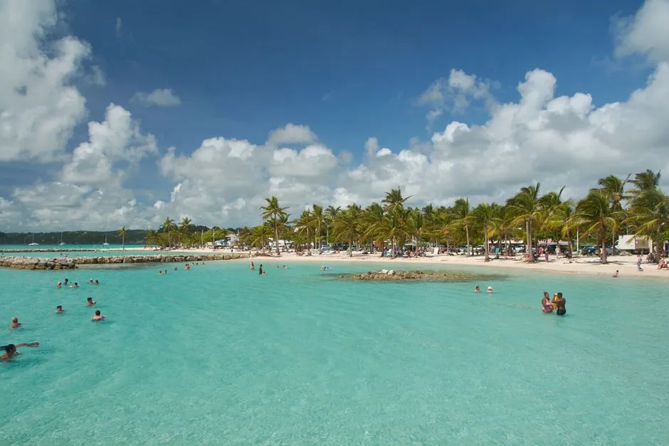 Plage de Sainte-Anne en Guadeloupe bondee de vacanciers, lagon turquoise et palmiers en pleine saison touristique