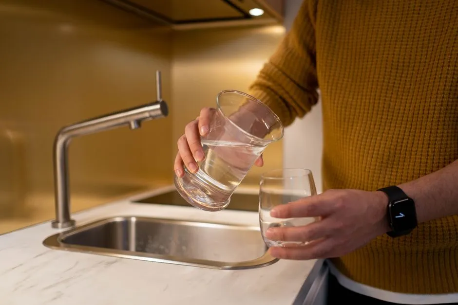 Personne remplissant un verre d'eau au robinet d'un évier de cuisine, illustrant la question de l'eau du robinet en Martinique