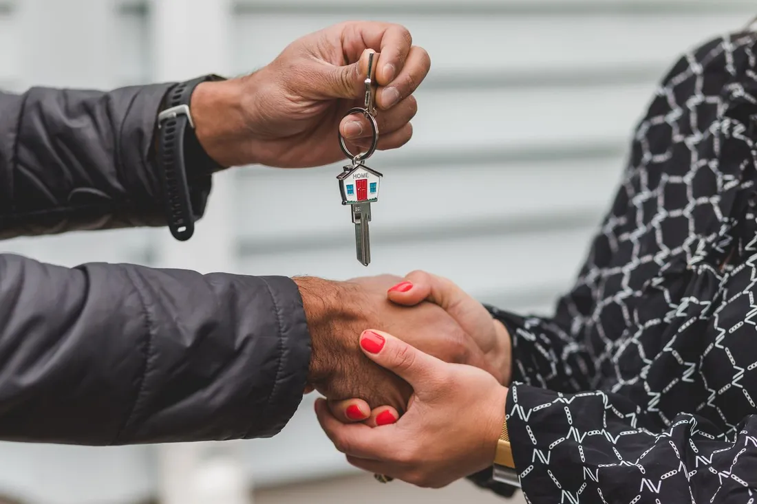 Remise des clés d'un logement avec porte-clés en forme de maison et poignée de main entre le propriétaire et la nouvelle locataire