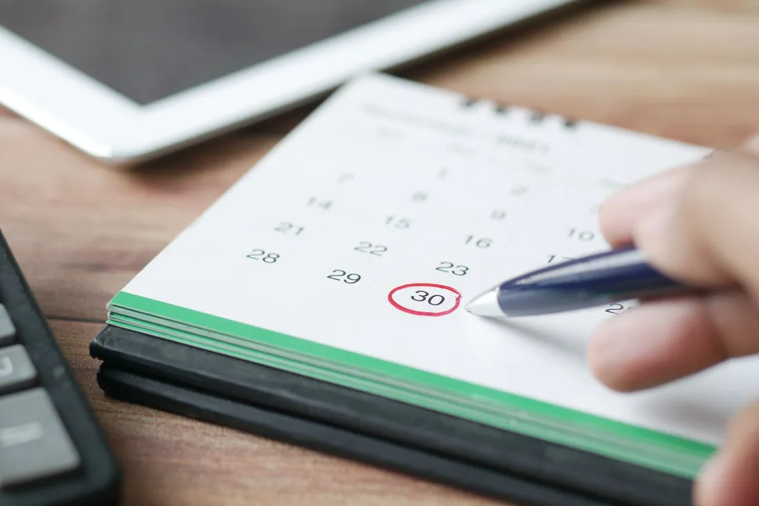 Main entourant au stylo une date sur un calendrier de bureau, posé près d'une tablette