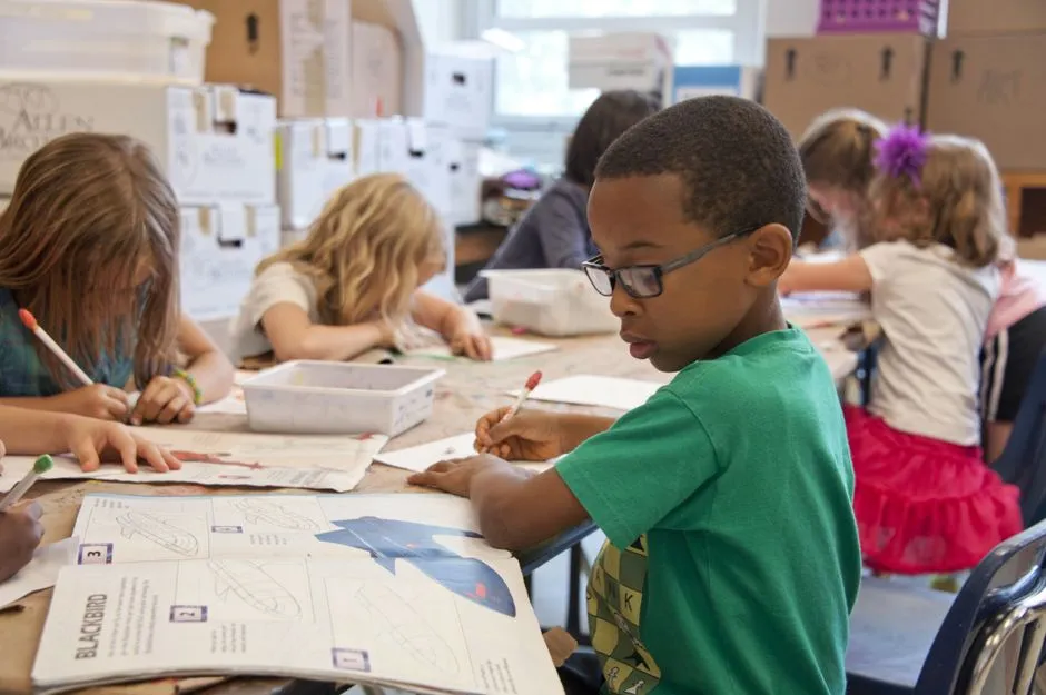 Élèves d'école élémentaire attablés en classe, occupés à écrire et dessiner sur leurs cahiers pendant une activité pédagogique