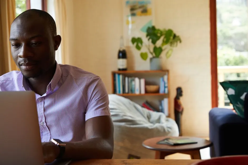 Homme en déplacement professionnel travaillant sur son ordinateur portable dans le séjour d'un appartement meublé, installation adaptée à une location longue durée