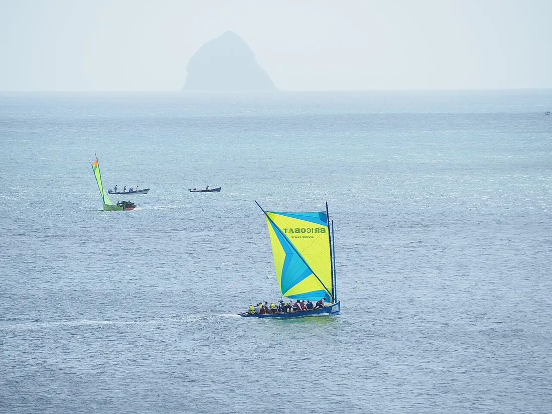 Yole ronde martiniquaise sous voile avec le rocher du Diamant en arrière-plan lors d'une course nautique
