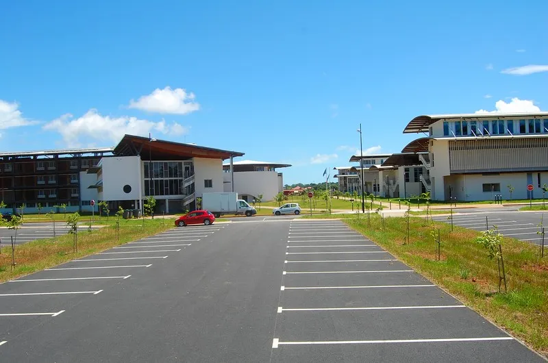 Bâtiments à toiture courbe et brise-soleil du Pôle universitaire guyanais et son parking, sur le campus de Troubiran à Cayenne
