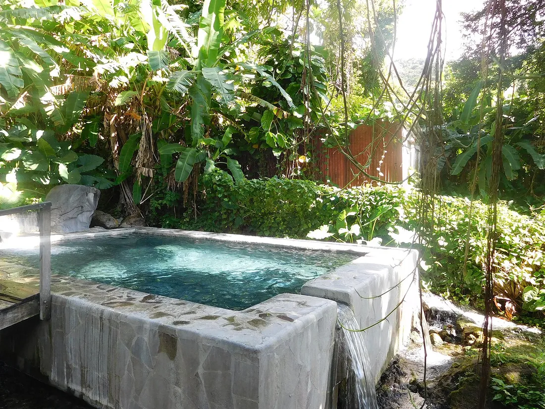 Le bassin de pierre des Bains de Dolé alimenté par une source chaude, entouré de bananiers et de végétation luxuriante en Guadeloupe