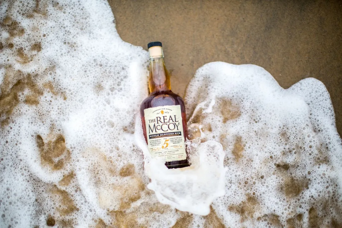 Bouteille de rhum vieux des Antilles posée sur le sable, baignée par l'écume des vagues
