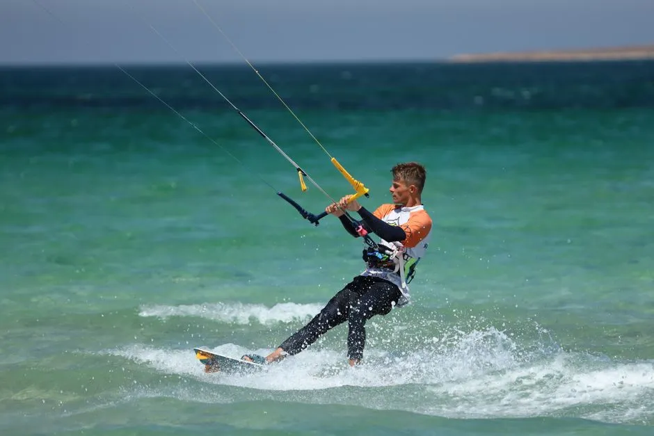 Kitesurfeur glissant sur une eau turquoise peu profonde, barre et lignes de l'aile tendues, dans une ambiance proche des spots de l'Atlantique martiniquais