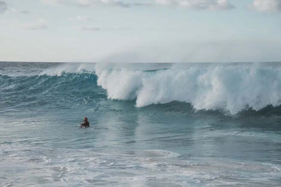 Surfeur dans le line-up face à une grosse vague qui déferle au large, eaux turquoise d'un spot de surf