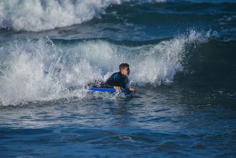 Bodyboardeur allongé sur sa planche bleue glissant dans l'écume d'une vague qui casse