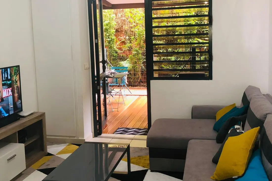 Living room of the Diamant Cayennais: grey corner sofa, coffee table and sliding door opening onto the terrace